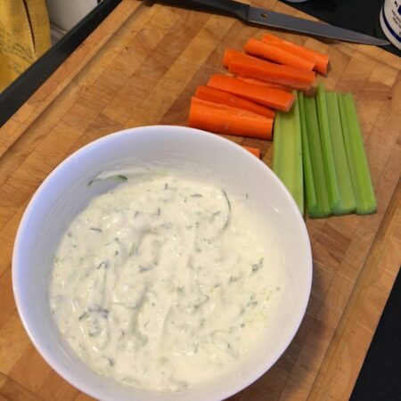 bowl of tzatziki dip on a chopping board with carrot and celery sticks