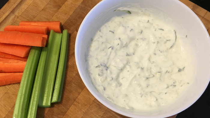 bowl of tzatziki dip on a wooden board with vegetable sticks