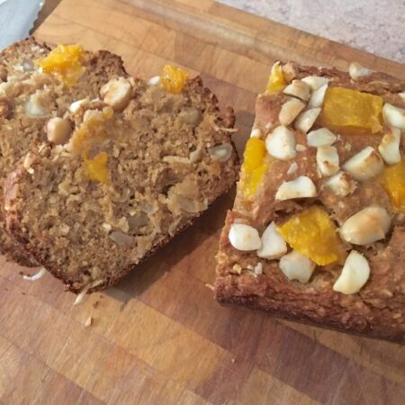 Mango macadamia loaf with a couple of slices cut on a chopping board