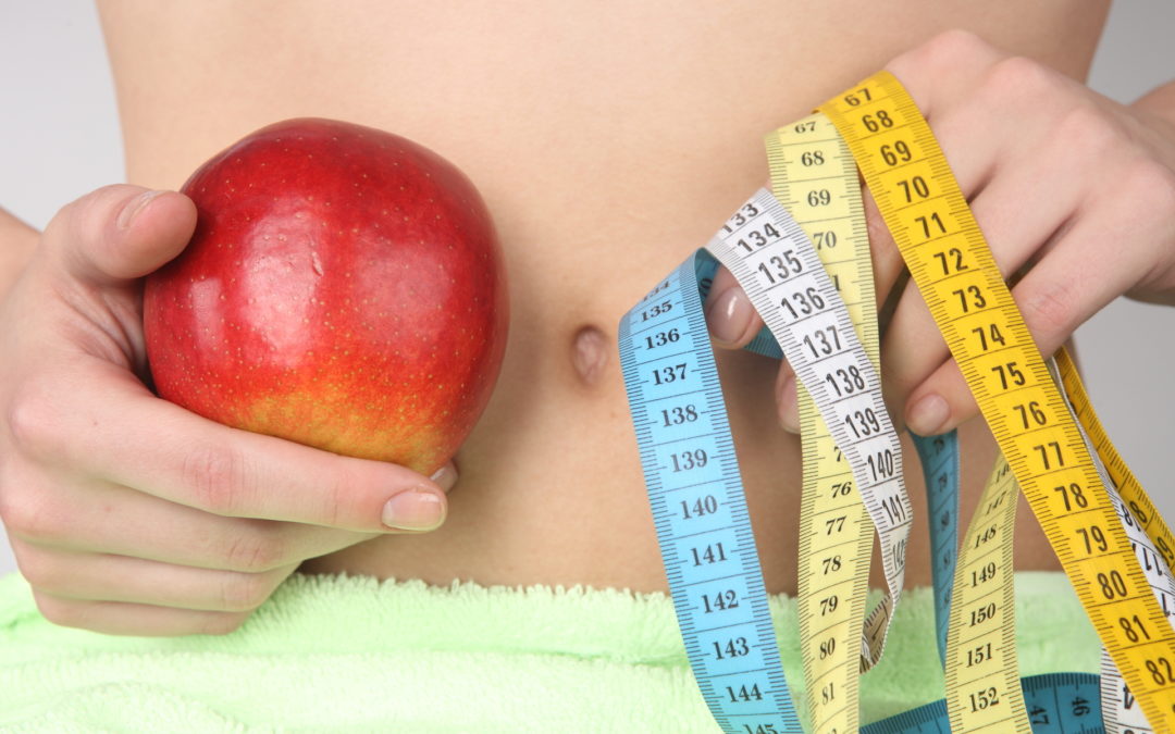 woman holding a tape measure and an apple in front of her bare stomach