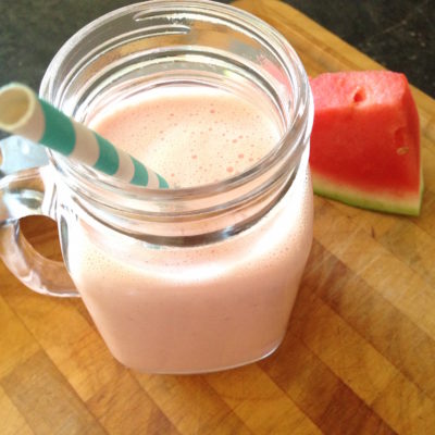 Strawberry watermelon smoothie in a mason jar with a straw. Sitting on a chopping board next to a chunk of watermelon