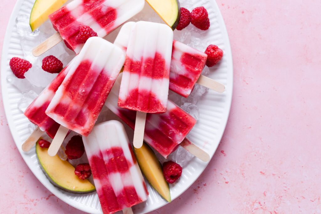 Mango raspberry coconut pops on a serving plate with fresh fruit