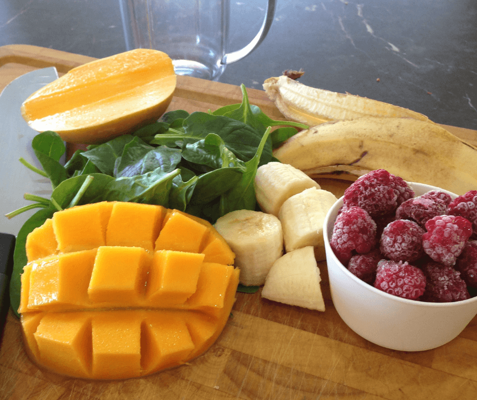 Smoothie ingredients on a chopping board: mango, banana, spinach, raspberries