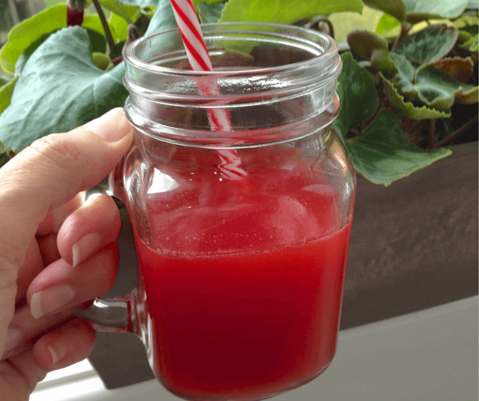 a red-green smoothie being held in a mason jar, with a plant in the background