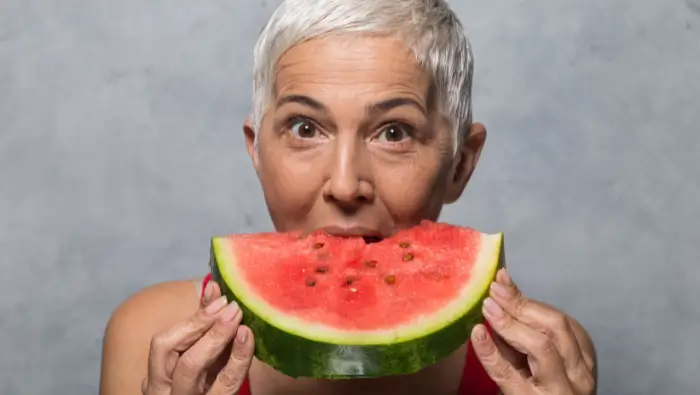 Close up of a woman biting into a large piece of watermelon