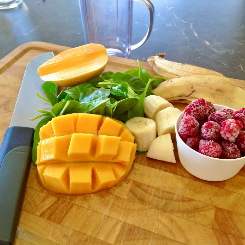 green smoothie ingredients on a bench next to a blender: mango, raspberries, banana and spinach