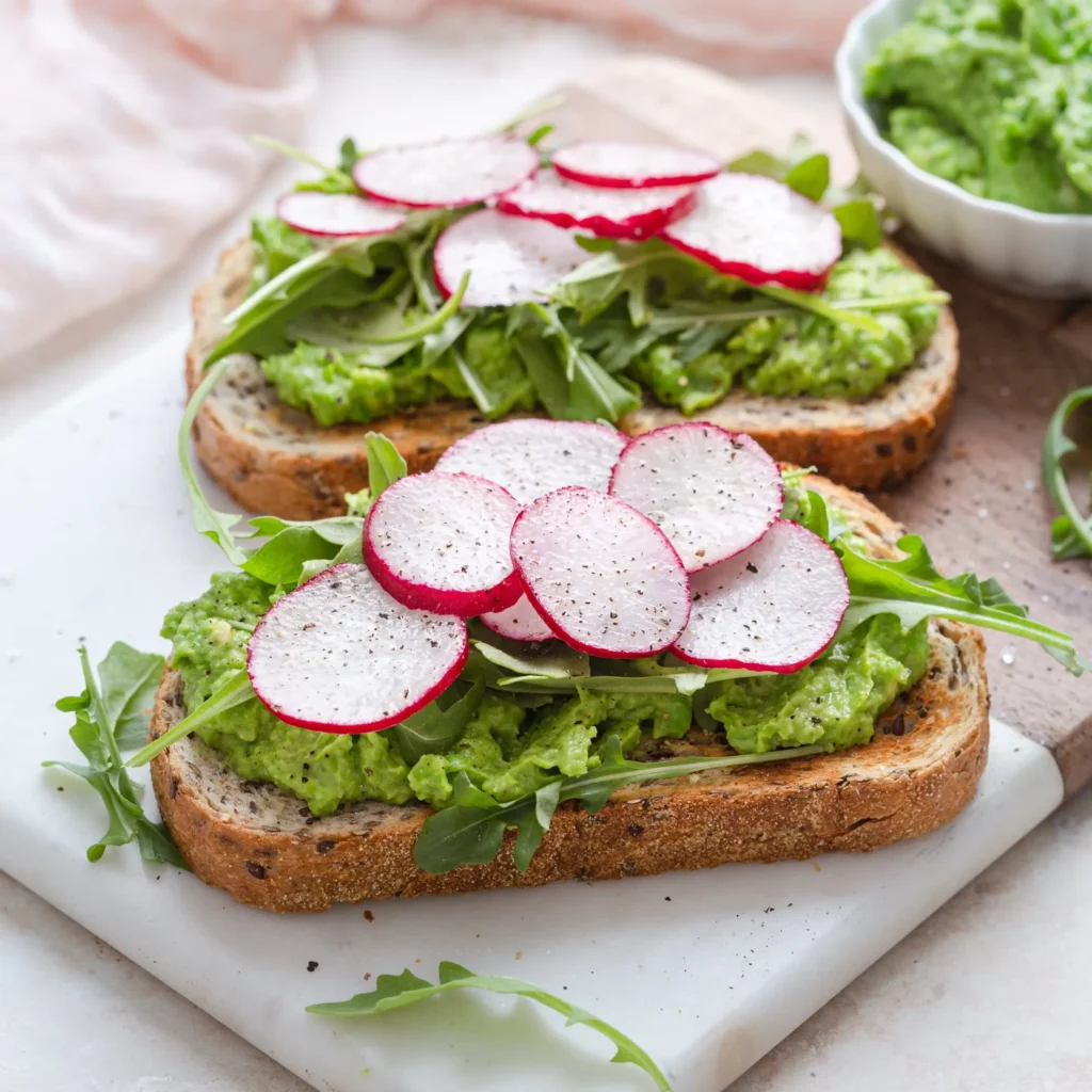 2 slices of toast with sweet pea and avocado spread, topped with sliced radishes